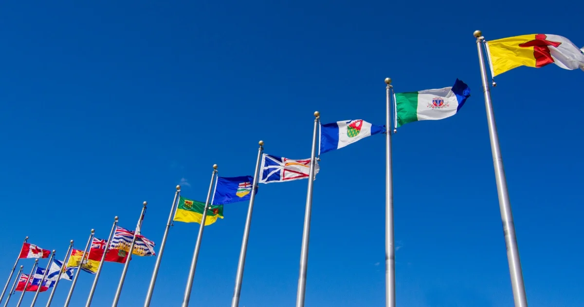 Canadian provincial and territorial flags flying on flagpoles under a clear blue sky